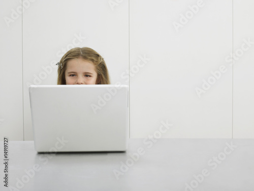 Photo: Small girl by desk using laptop Small girl by desk using laptop