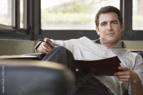 Photo: Relaxed portrait of successful mid adult businessman reclining on sofa with folder Relaxed portrait of successful mid adult businessman reclining on sofa with folder