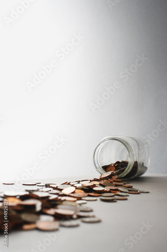 Photo: Coins spilling out of jar on its side, in studio Coins spilling out of jar on its side, in studio