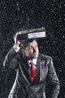Businessman covering head with binder, running through rain