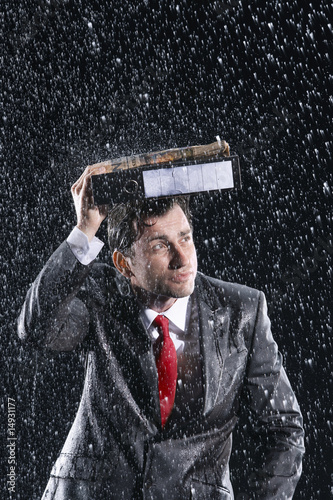 Photo: Businessman covering head with binder, running through rain Businessman covering head with binder, running through rain