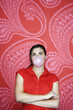 Teenaged girl blowing bubble against pink and red patterned wallpaper