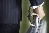 Photo: Middle-aged businessman handcuffed to briefcase, mid section, close-up, back view Middle-aged businessman handcuffed to briefcase, mid section, close-up, back view