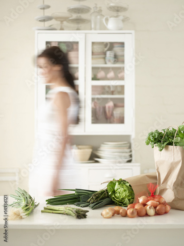 Photo: Woman walking behind Fresh Produce on Kitchen Counter, side view Woman walking behind Fresh Produce on Kitchen Counter, side view