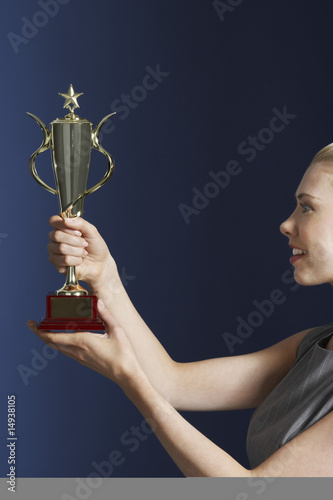 Photo: Woman holding and admiring trophy against dark background, profile Woman holding and admiring trophy against dark background, profile