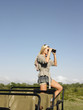 Photo: Young woman on safari, standing in jeep, looking through binoculars, side view Young woman on safari, standing in jeep, looking through binoculars, side view