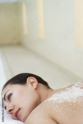 Photo: Young woman with salts on back lying on massage table, portrait Young woman with salts on back lying on massage table, portrait