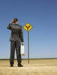 Businessman looking at road sign in desert, back view