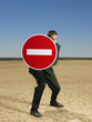 Businessman holding 'no entry' sign in desert, full length