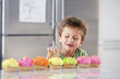 Young boy picking decoration off cupcake in kitchen