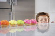 Young boy peeking over counter at row of cupcakes in kitchen