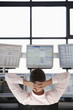 Businessman with Hands Behind Head, watching computer screens, back view.