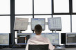 Businessmen sitting at desk, watching computer screens, back view.