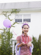 Foto: Girl 10-12 in feather boa holding balloon outside house Girl 10-12 in feather boa holding balloon outside house