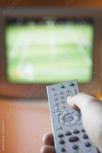 Photo: Man changing TV channel with remote control, close-up on hand Man changing TV channel with remote control, close-up on hand
