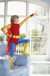 Young boy 7-9 wearing superman costume standing on armchair and pointing