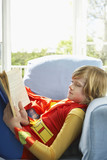 Photo: Young boy 7-9 sitting in armchair reading, wearing superhero costume, side view Young boy 7-9 sitting in armchair reading, wearing superhero costume, side view