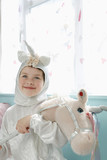 Photo: Portrait of young girl 5-6 in unicorn costume holding toy horse, smiling, indoors Portrait of young girl 5-6 in unicorn costume holding toy horse, smiling, indoors