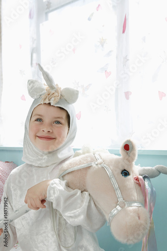 Photo: Portrait of young girl 5-6 in unicorn costume holding toy horse, smiling, indoors Portrait of young girl 5-6 in unicorn costume holding toy horse, smiling, indoors