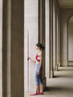 Foto: Female athlete holding javelin, standing in portico, side view Female athlete holding javelin, standing in portico, side view