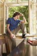 Young man sitting on sill looking out living room window