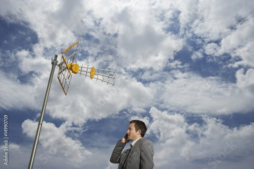 Foto: Business man using cell phone underneath satellite tower Business man using cell phone underneath satellite tower