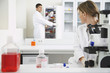 Photo: Scientist using microscope with second scientist getting specimen in laboratory Scientist using microscope with second scientist getting specimen in laboratory