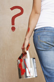 Photo: Woman holding painting can facing wall with painted question mark, mid section, back view Woman holding painting can facing wall with painted question mark, mid section, back view