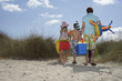Parents and three children 6-11 carrying beach accessories, back view