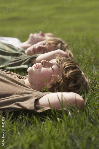 Foto: Three teenage brothers 13-17 lying down on front lawn, close up Three teenage brothers 13-17 lying down on front lawn, close up