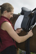 Girl tightening saddle on horse