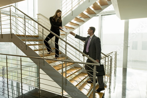 Photo: Businesswoman and businessman exchanging document on office staircase Businesswoman and businessman exchanging document on office staircase