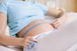 Pregnant woman measuring stomach on bed