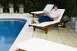 Young man on chaise lounge by pool reading
