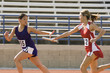 Female track athlete passing relay baton to another one