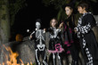 Girls and boys 7-9 wearing Halloween costumes, cooking marshmallows on campfire