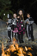 Girls and boys 7-9 wearing Halloween costumes, cooking marshmallows on campfire