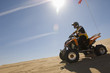 young man riding atv over sand dune