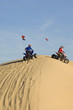 young men riding atvs over sand dunes