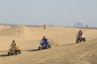 three young men riding atvs on dunes