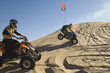 young men riding atvs over sand dunes