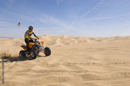 Photo: young man riding atv over sand dune young man riding atv over sand dune