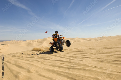 Photo: young man riding atv over sand dune young man riding atv over sand dune