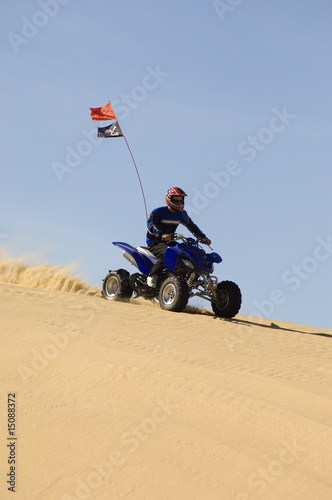 Photo: young man riding atv over sand dune young man riding atv over sand dune
