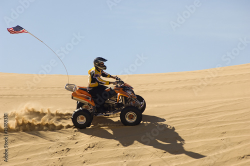 Photo: young man riding atv over sand dune young man riding atv over sand dune