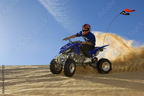 Photo: young man riding atv over sand dune young man riding atv over sand dune