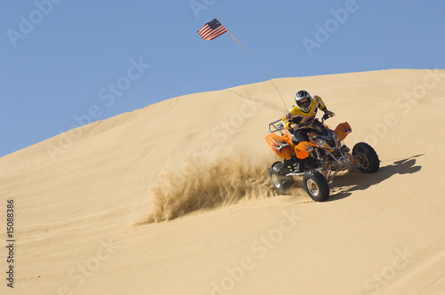 Photo: young man riding atv over sand dune young man riding atv over sand dune