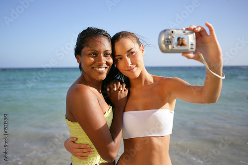 Photo: Jeunes femmes souriantes au bord de la plage se photographiant Jeunes femmes souriantes au bord de la plage se photographiant