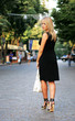 The harmonous blonde on heels walks on a cobblestone road