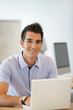 Homme souriant assis à un bureau devant un ordinateur portable
